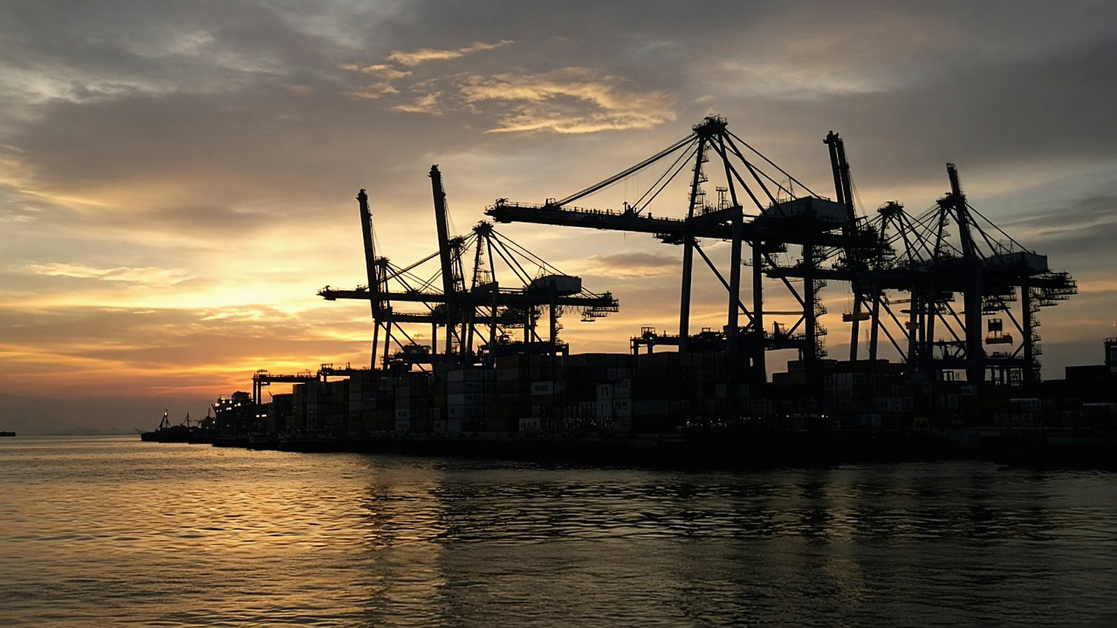 Container port with ship-to-shore gantry cranes silhouetted at sunset